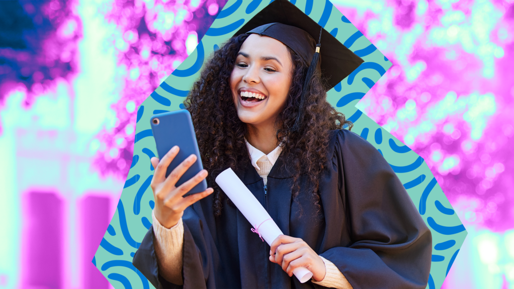 A college graduate in a cap and gown happily looking at her phone while holding a diploma.