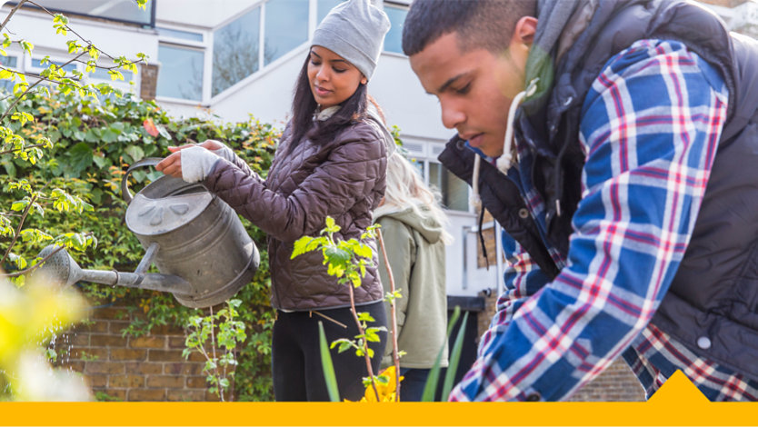Two volunteers tend to a flower bed outside a corporate office.