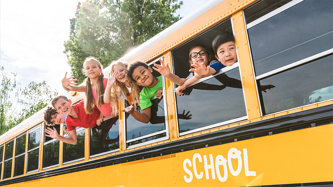 A group of primary school children waving out the windows of a school bus