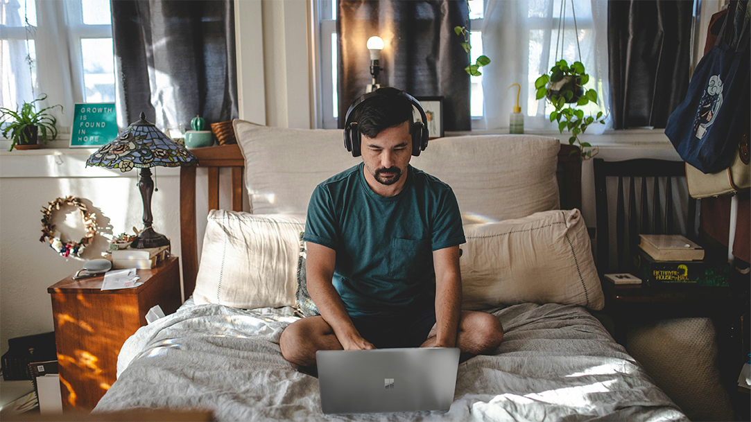 A man with headphones on a computer in his bedroom