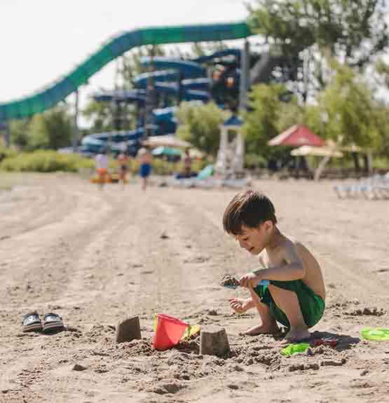 enfant qui joue avec sceau et sable sur une plage avec glissades derrière