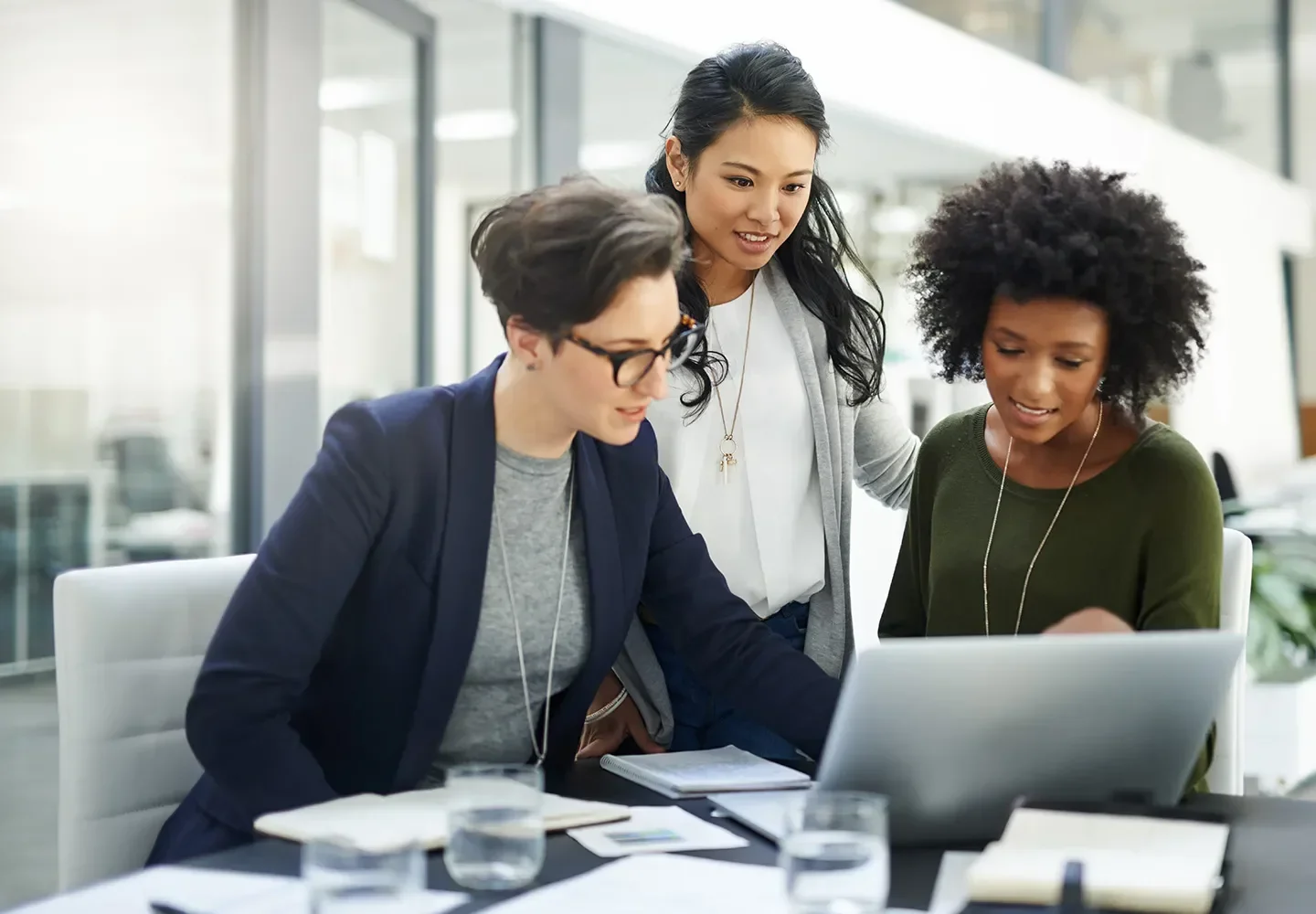 Three businesswomen hovering over a laptop discussing customer experience strategy
