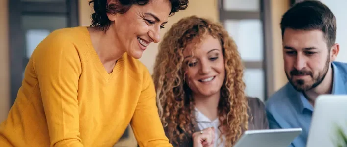 Three cheerful people collaboratively looking at a tablet in a bright, modern setting.
