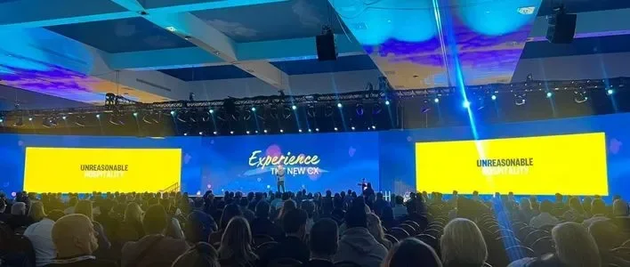 Conference setting with a large audience and colorful stage backdrop.
