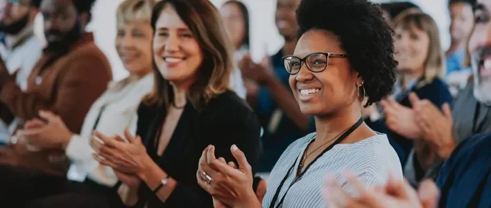 A diverse group of people smiling and clapping, showing enthusiasm and support.