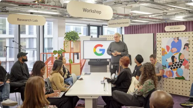Ten Googlers sit around a table at the Accessibility Discovery Centre, a man stands speaking at the end of it 